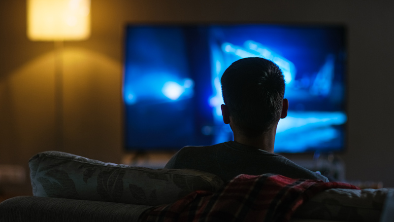 boy facing the television watching it in the dark